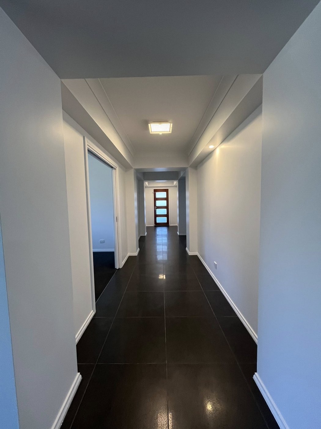 Hallway with black tile flooring leading to front door