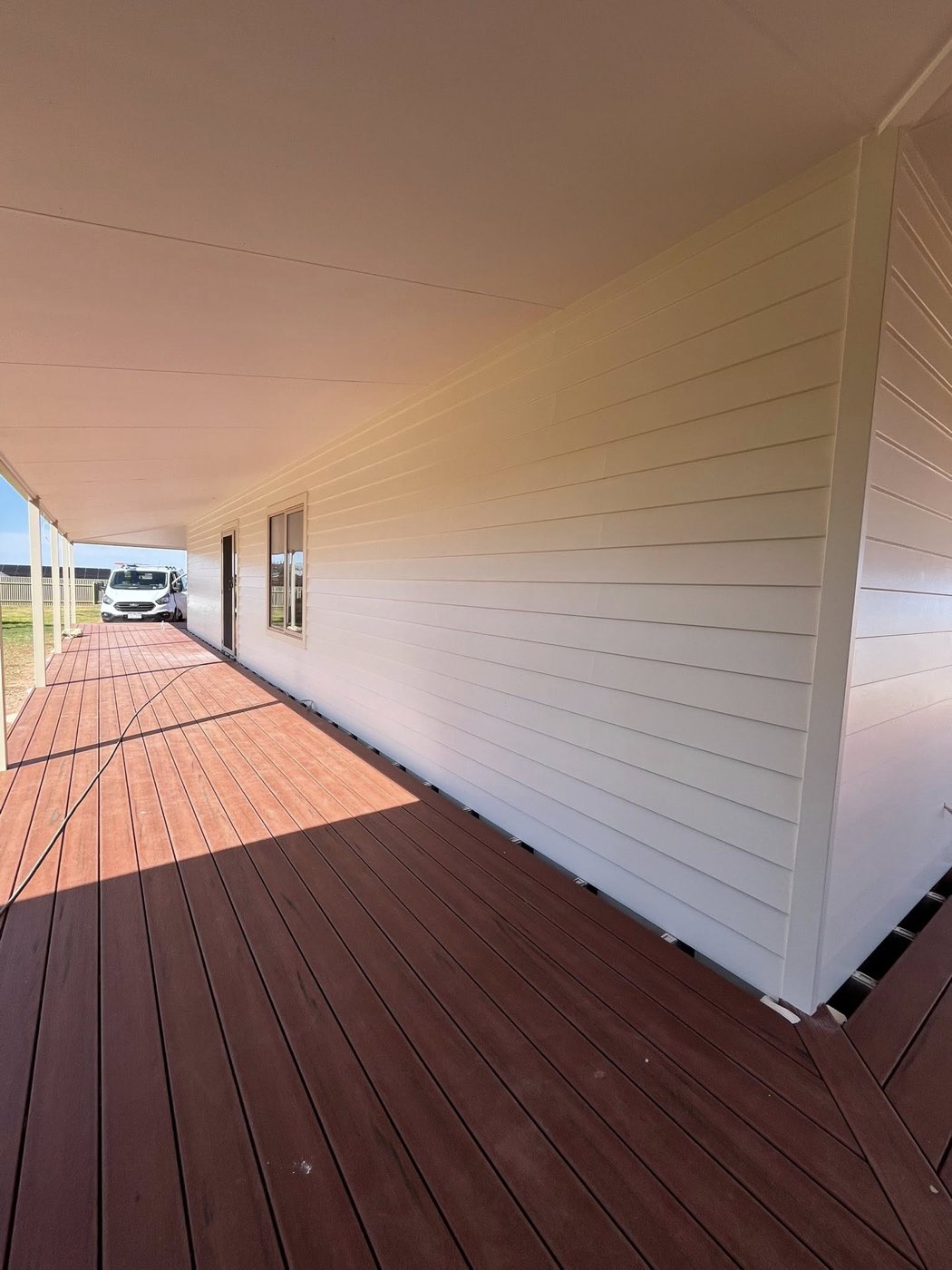 Long verandah with white weatherboard and stained timber deck